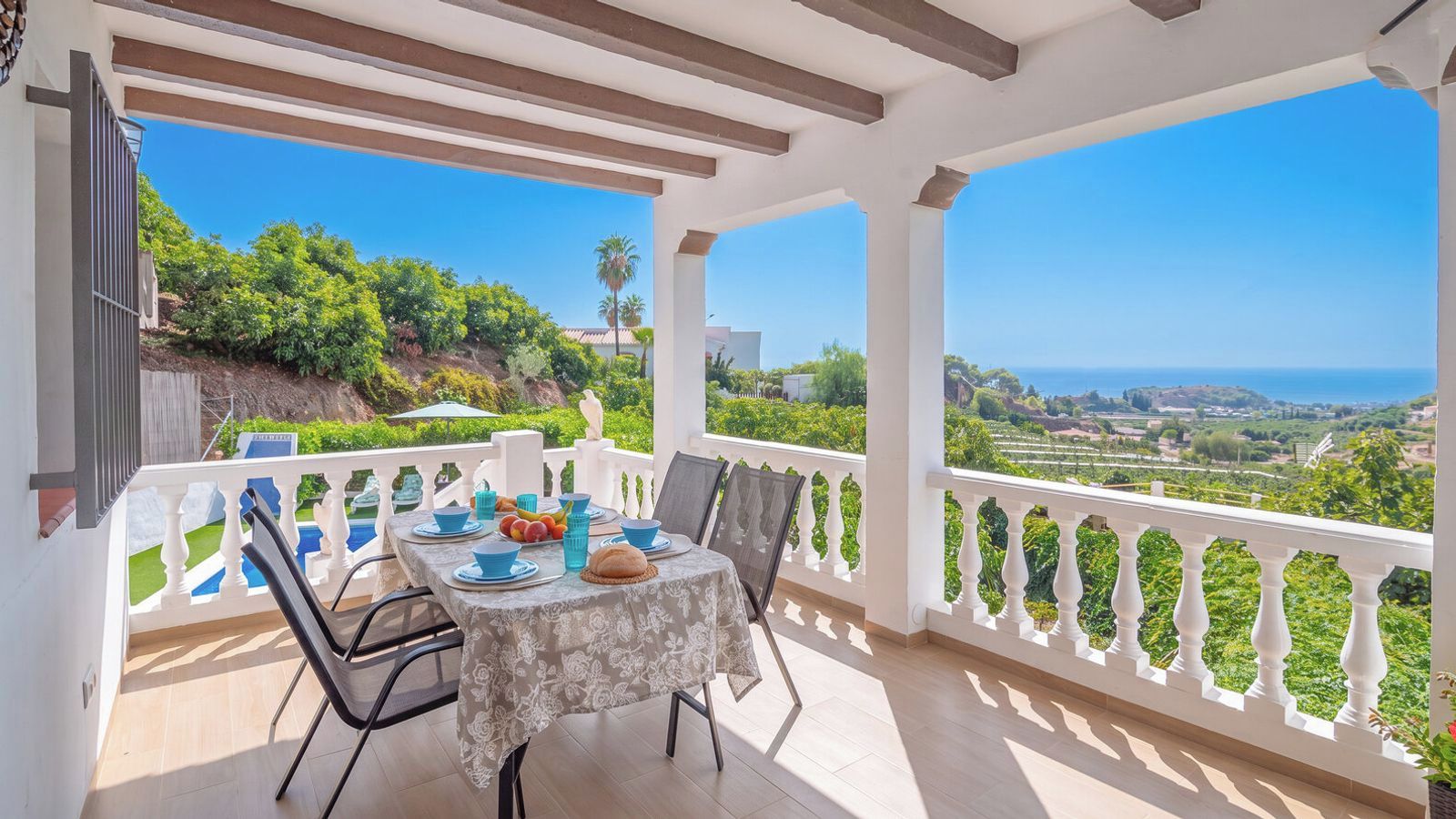 A covered outdoor dining area with a table set for two, overlooking a scenic landscape.