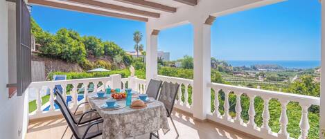 A covered outdoor dining area with a table set for two, overlooking a scenic landscape.