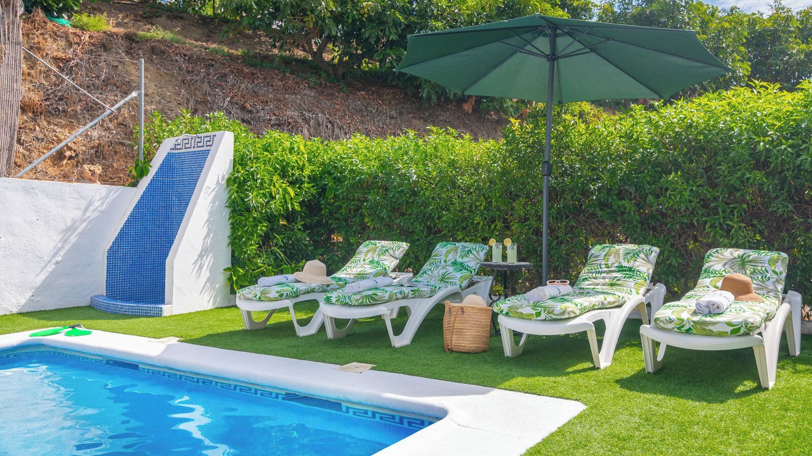 Un espace aménagé au bord de la piscine, avec un toboggan, des chaises longues et une table où sont servis des boissons.