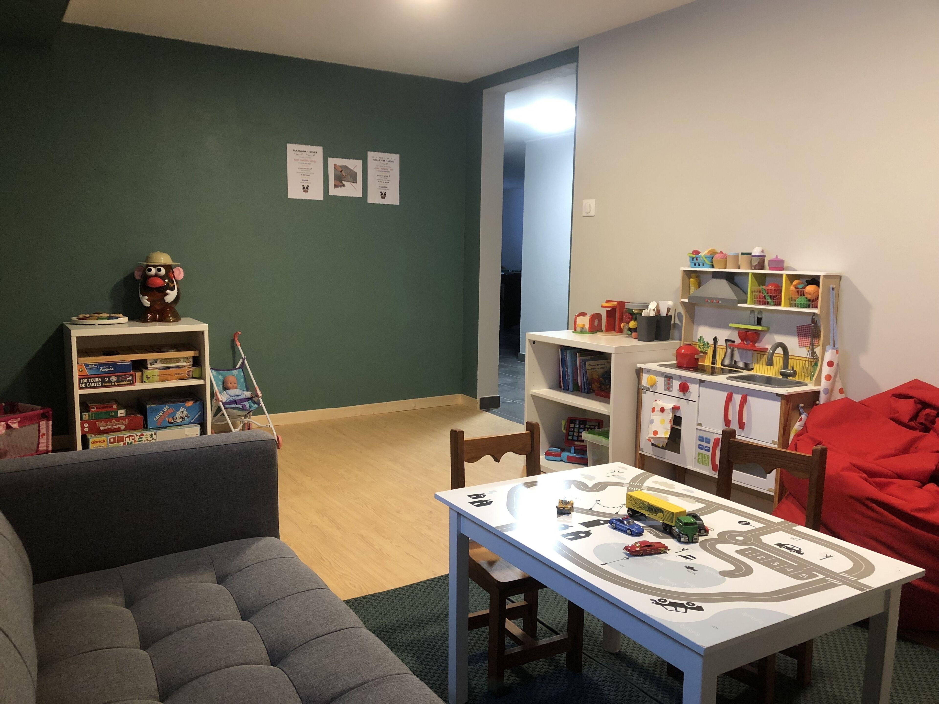 Ein Wohnzimmer mit grauem Sofa, einem kleinen Tisch mit Spielzeug und einem Bücherregal.