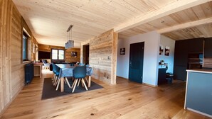 Een ruime kamer met houten vloer en plafond, een eethoek met tafel en stoelen, en een keuken met kasten en apparatuur.