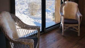 Een kamer met een grote schuifglazen deur die uitkomt op een besneeuwde omgeving, rieten stoelen en houten vloeren.