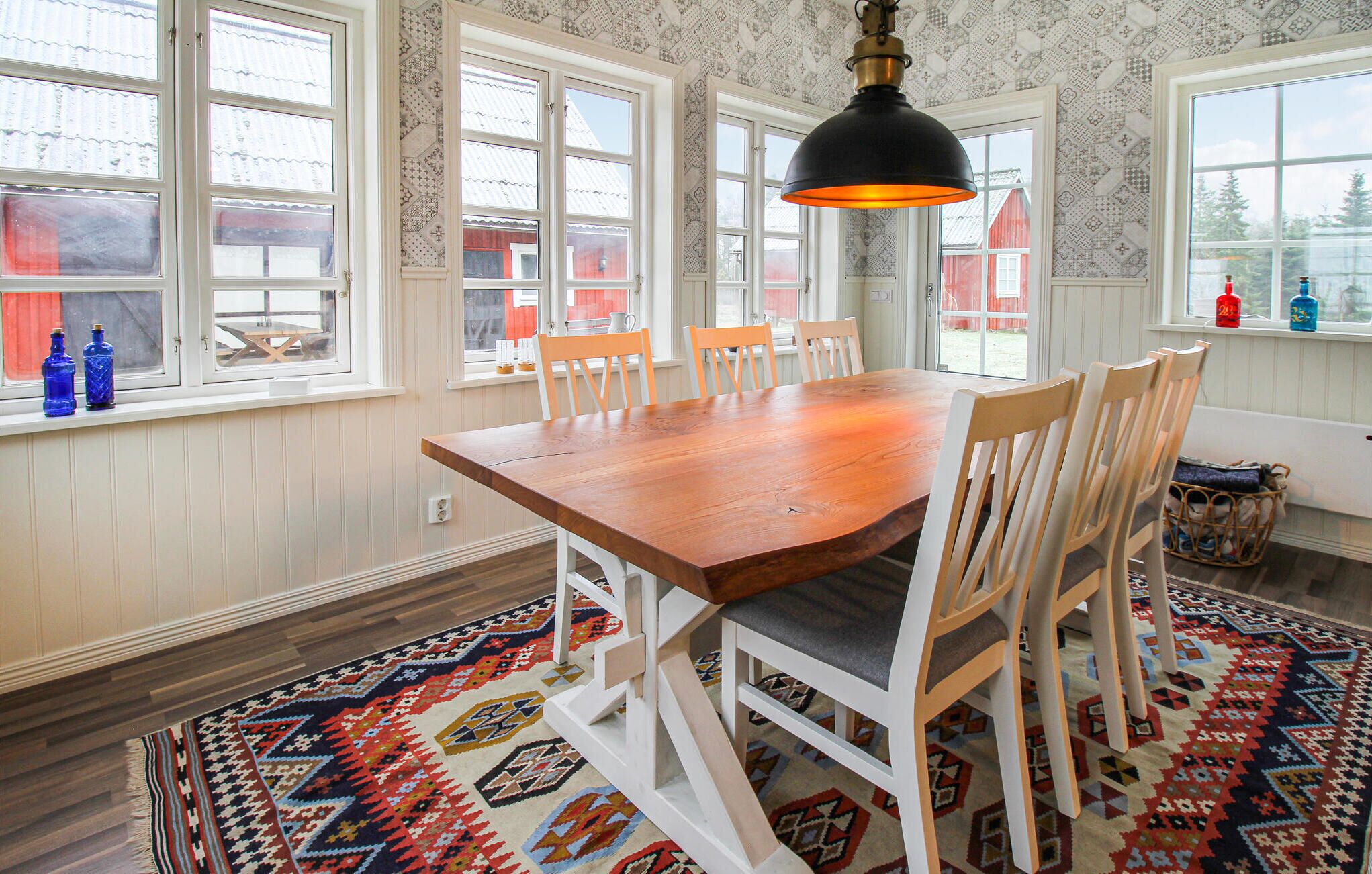 Uma sala de jantar com mesa de madeira e cadeiras brancas, papel de parede estampado e um tapete.