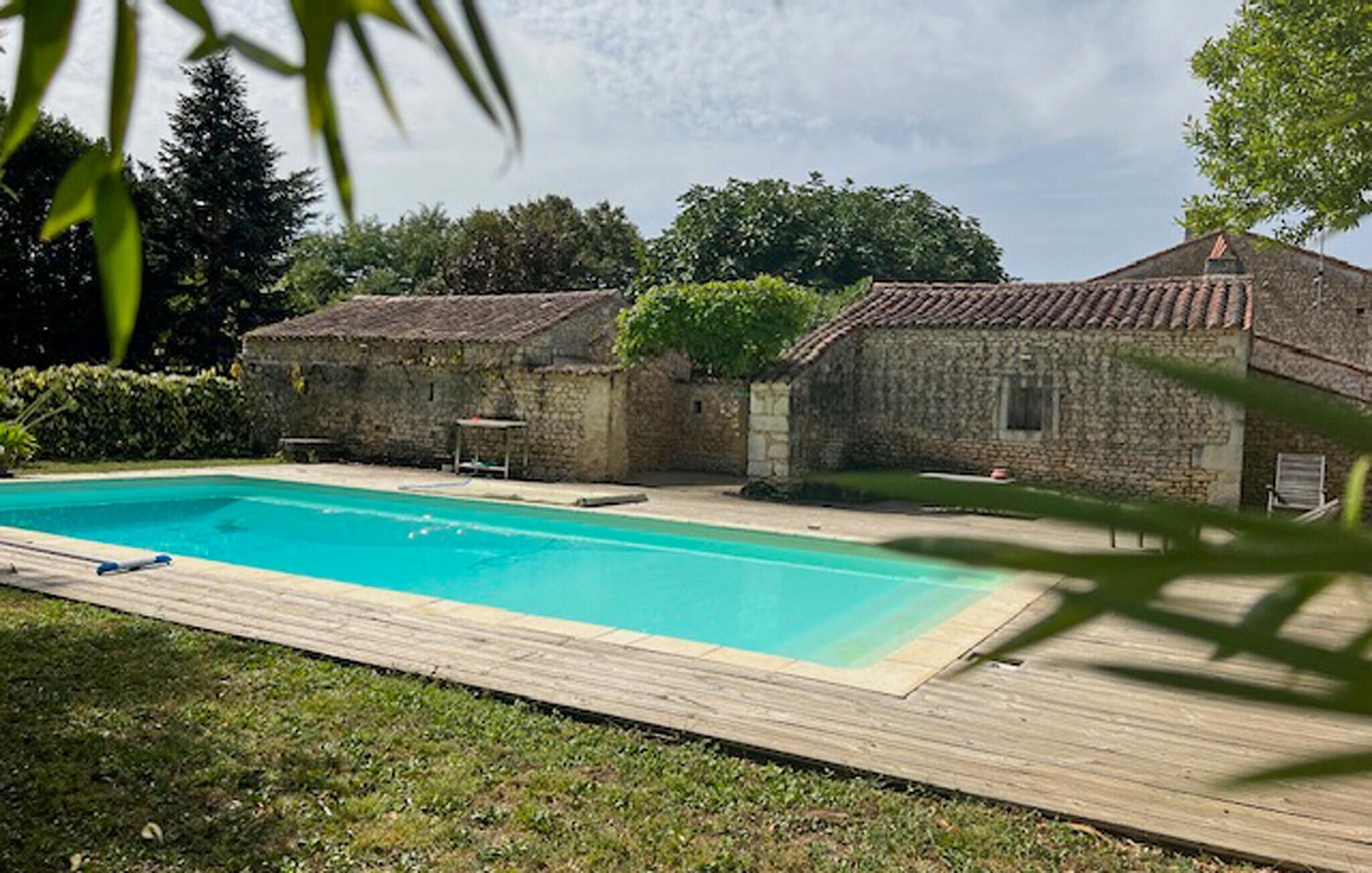 Una piscina con cubierta de madera, rodeada de edificios de piedra y vegetación.