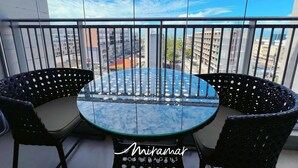 Varanda com mesa de vidro redonda e duas cadeiras, com vista para a paisagem urbana.
