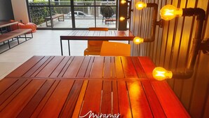 Mesa e cadeiras de madeira em um quarto moderno, bem iluminado, com janelas grandes e vista para o exterior.