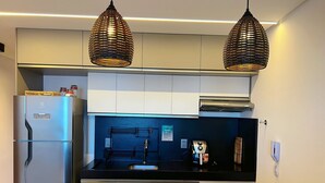 Uma cozinha moderna com duas luminárias pendentes, uma geladeira embutida e um balcão preto com duas xícaras e pires brancos.