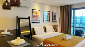 Quarto de hotel com cama, mesa de cabeceira e duas luzes pendentes. Há duas obras de arte emolduradas na parede, uma janela com cortinas e vista para edifícios.