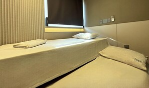 Una habitación pequeña con cama individual, ventana, mesita de noche y teléfono instalado en la pared.