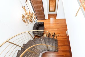 Stunning staircase with a curved design and ornate chandelier, complemented by a leather bench and polished wooden floor.