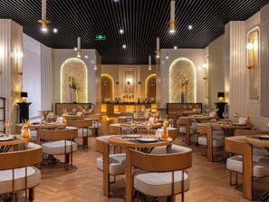 Ein Restaurantinnenraum mit runden Tischen, gepolsterten Stühlen und einem modernen Deckenstil.