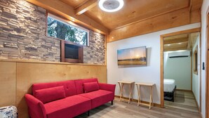 A modern room with a red sofa, stone wall, wooden ceiling, and a painting. - Find Peace - Tiny House in Japanese Garden (Homestead)