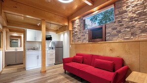 A modern interior with a red sofa, wooden flooring, stone wall, and a kitchen area. - Find Peace - Tiny House in Japanese Garden (Homestead)