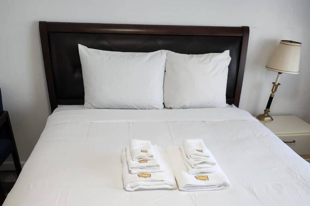 A neatly made bed with white linens and towels, a dark wooden headboard, and a bedside lamp.
