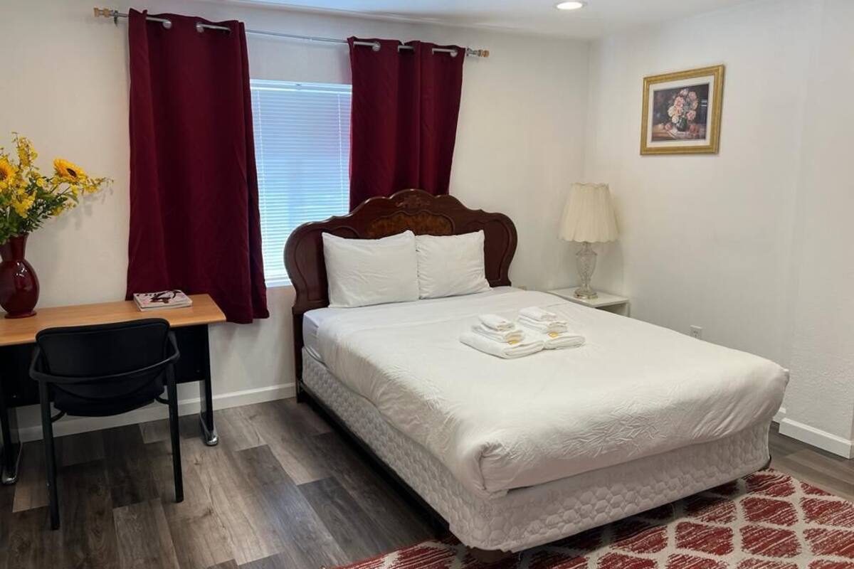 A hotel room with a bed, a desk, a chair, a lamp, and a picture on the wall.