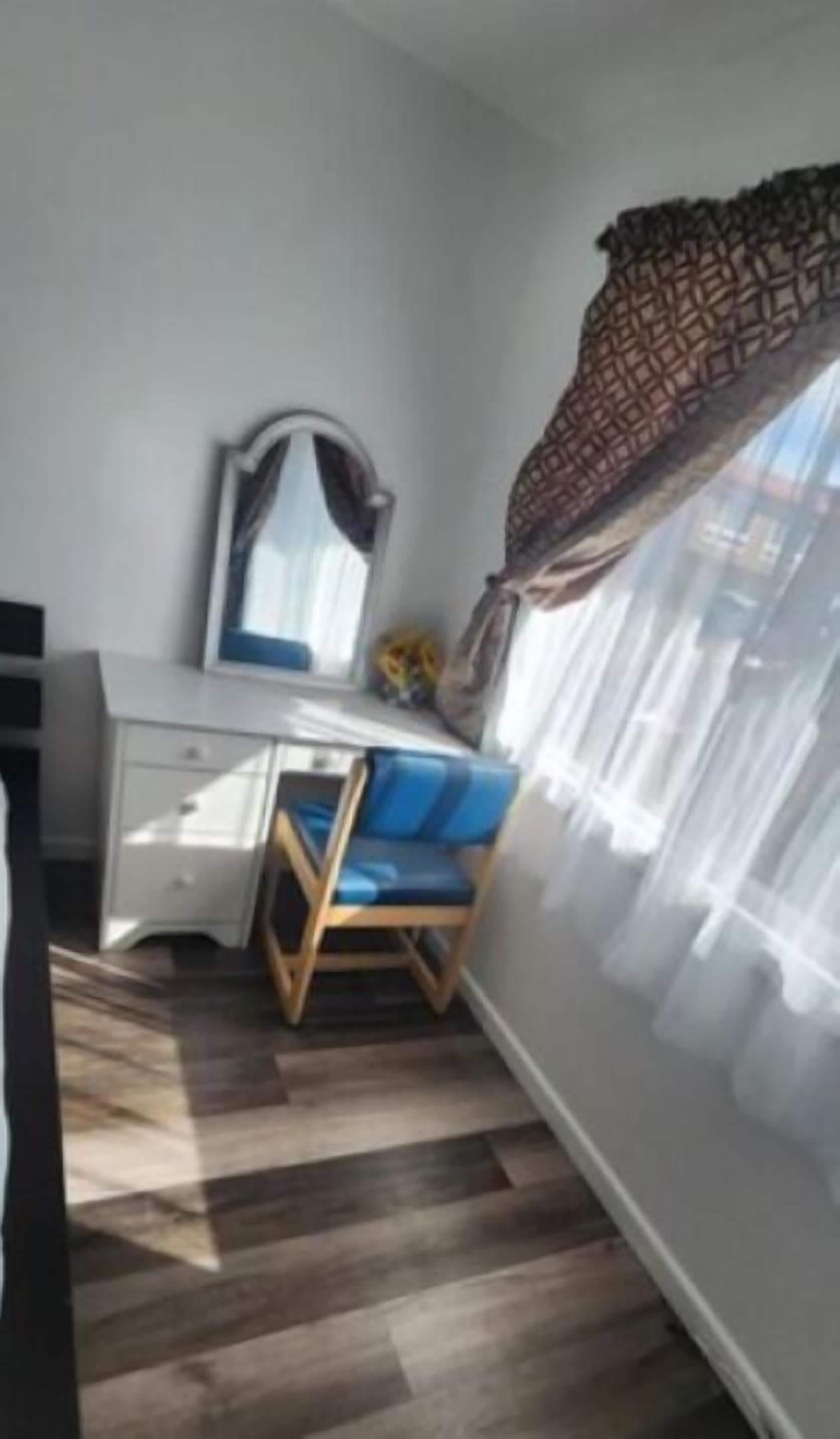 Huone, jossa on työpöytä, tuoli ja ikkuna, jossa on ohuet verhot.