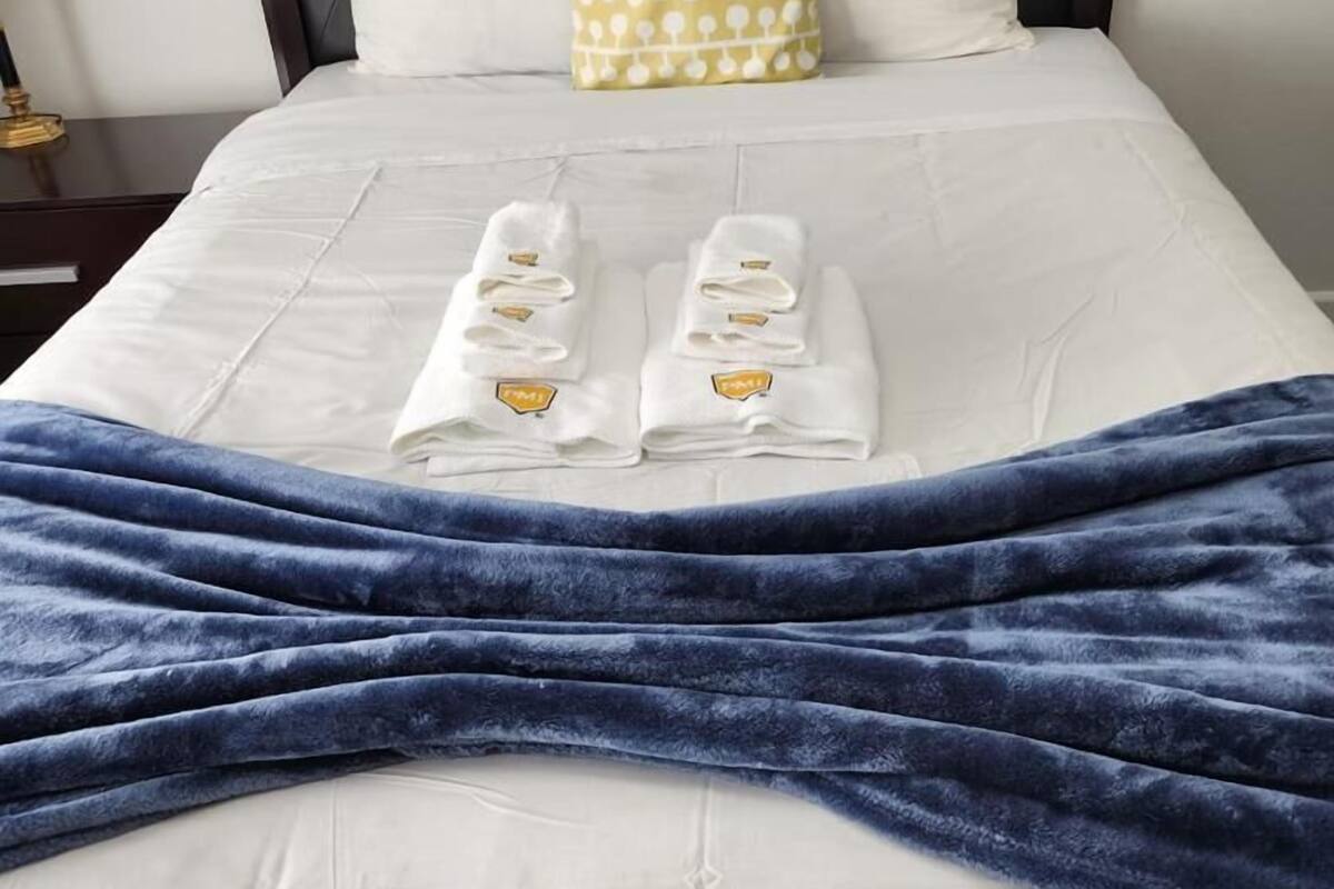 A neatly made bed with white linens, a blue blanket, and two towels with a gold emblem.