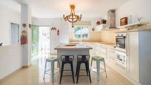 A modern kitchen with a central island, bar stools, a chandelier, and a view of the outdoors. - Luxurious home in Viñuela (Viñuela)