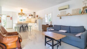 A modern living room with a sofa, coffee table, and leather armchair. There is a kitchen area with a refrigerator, stove, and bar stools. - Luxurious home in Viñuela (Viñuela)