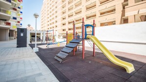 En utomhuslekplats med en gul rutschkana, klätterställningar och en bänk.