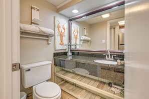 A bathroom with a toilet, sink, and mirror. There are towels on a shelf and a lobster decoration on the wall. - Oceanfront Balcony: Resort Condo in Myrtle Beach (Myrtle Beach)