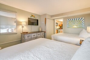 A hotel room with two beds, a wooden dresser, a flat-screen TV, a decorative wall piece, and a view into the kitchen area. - Oceanfront Balcony: Resort Condo in Myrtle Beach (Myrtle Beach)