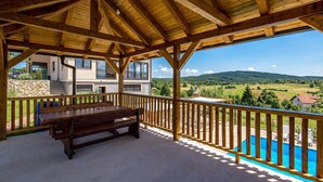 A covered outdoor area with a wooden bench, a pool, and a view of a house and landscape. - Beautiful apartment in Rakovica with WiFi (Rakovica)
