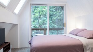 A bedroom with a large bed, skylight windows, and a view of trees outside.
