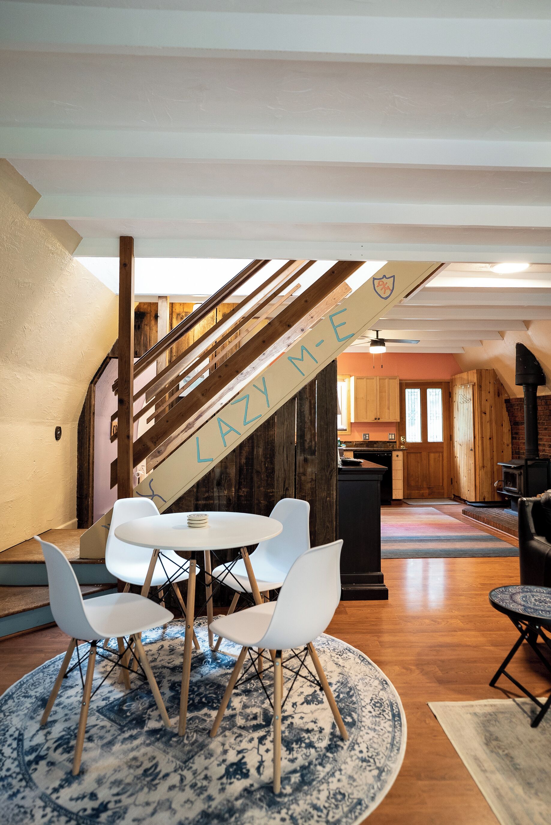 Un intérieur chaleureux avec un escalier, un coin repas avec des chaises blanches et une cuisine en arrière-plan.