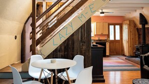 A cozy interior with a staircase, a dining area with white chairs, and a kitchen in the background.