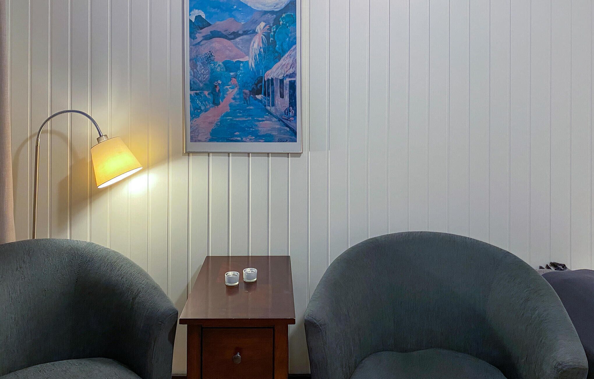 Una stanza con due poltrone, un tavolino in legno con due tazze, una lampada da terra e un quadro appeso al muro.