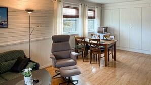 Une pièce avec un plancher en bois, une table à manger avec des chaises, un canapé, une lampe sur pied et un téléviseur posé sur un meuble.