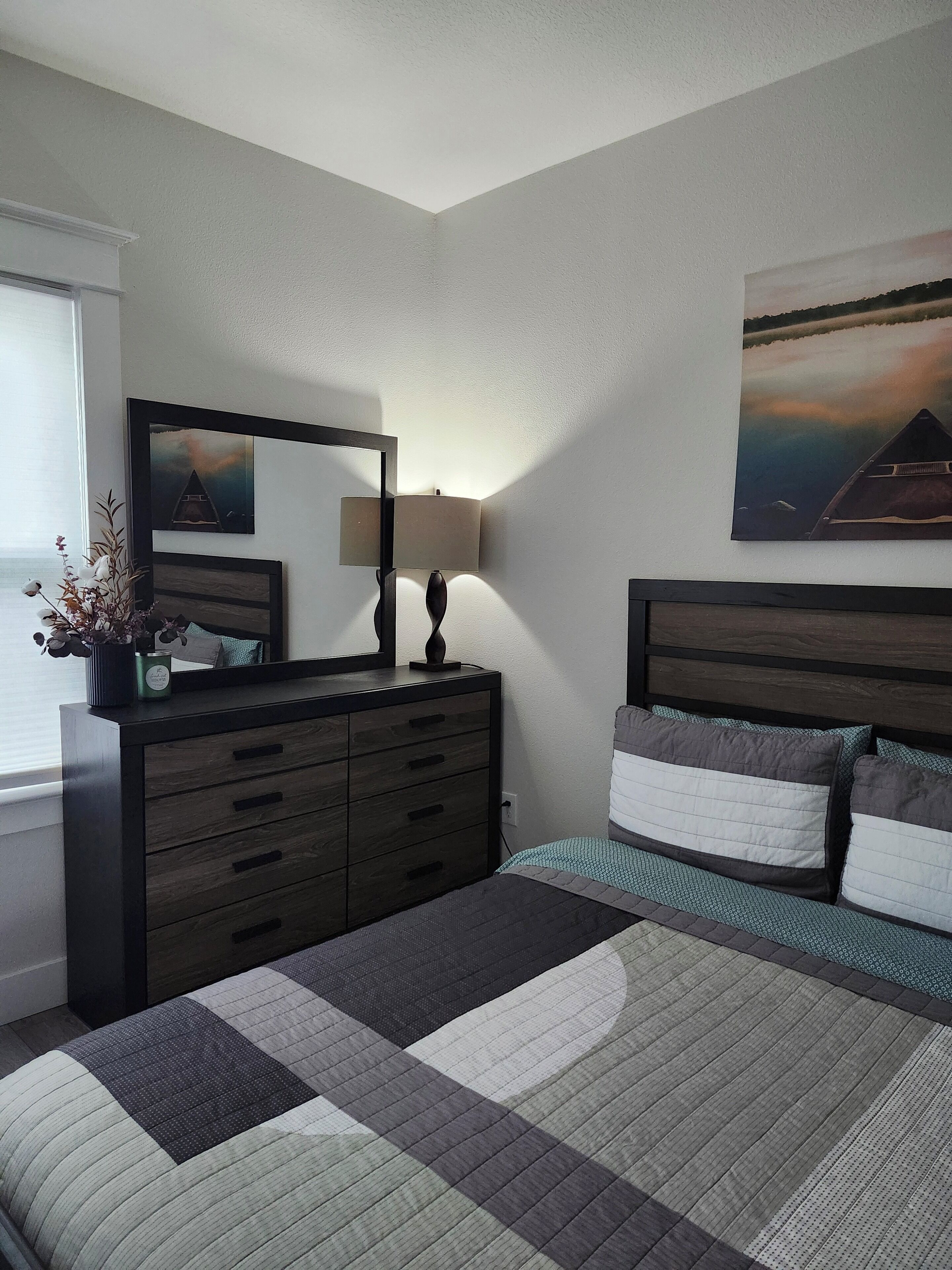 A bedroom with a bed, a dresser, a mirror, and two paintings on the wall.