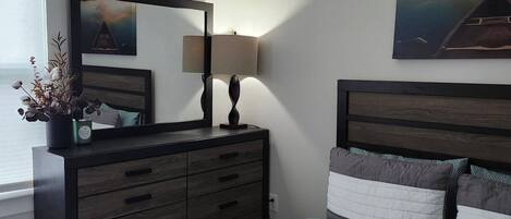 A bedroom with a bed, a dresser, a mirror, and two paintings on the wall.