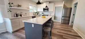 Cozinha moderna com ilha central, armários brancos e eletrodomésticos de aço inoxidável.
