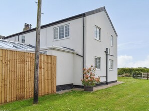 A two-story house with a flat roof, a wooden fence, and a small garden with flowers. - 5 bedroom accommodation in Warton, near Lytham (Warton, near Lytham)