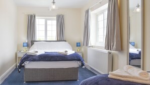 Ein Schlafzimmer mit einem Bett, Nachttischlampen, einem Spiegel und einem Fenster mit Vorhängen.