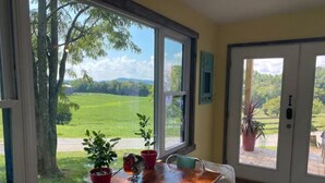 A dining area with a table and chairs, large windows with a view of a green landscape, and a door leading outside. - Adorable one bedroom with fireplace/kitchenette (Raywick)