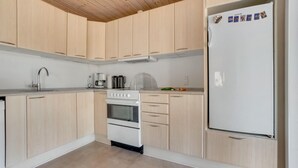A modern kitchen with light wood cabinets, a white refrigerator, a stove, and a sink.