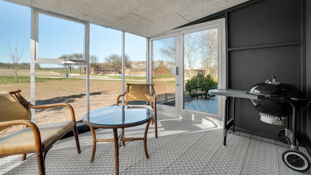 A sunroom with a glass door, a round table, two chairs, and a barbecue grill.