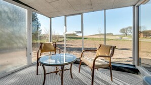 A room with a glass table and two chairs, large windows, and a view of a golf course.