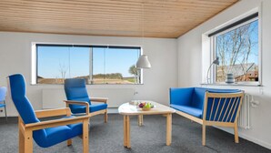 A modern living room with a view of the countryside, featuring blue upholstered chairs, a wooden coffee table, and a blue sofa.