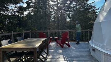 A wooden deck with a table and chairs, overlooking a forested area.