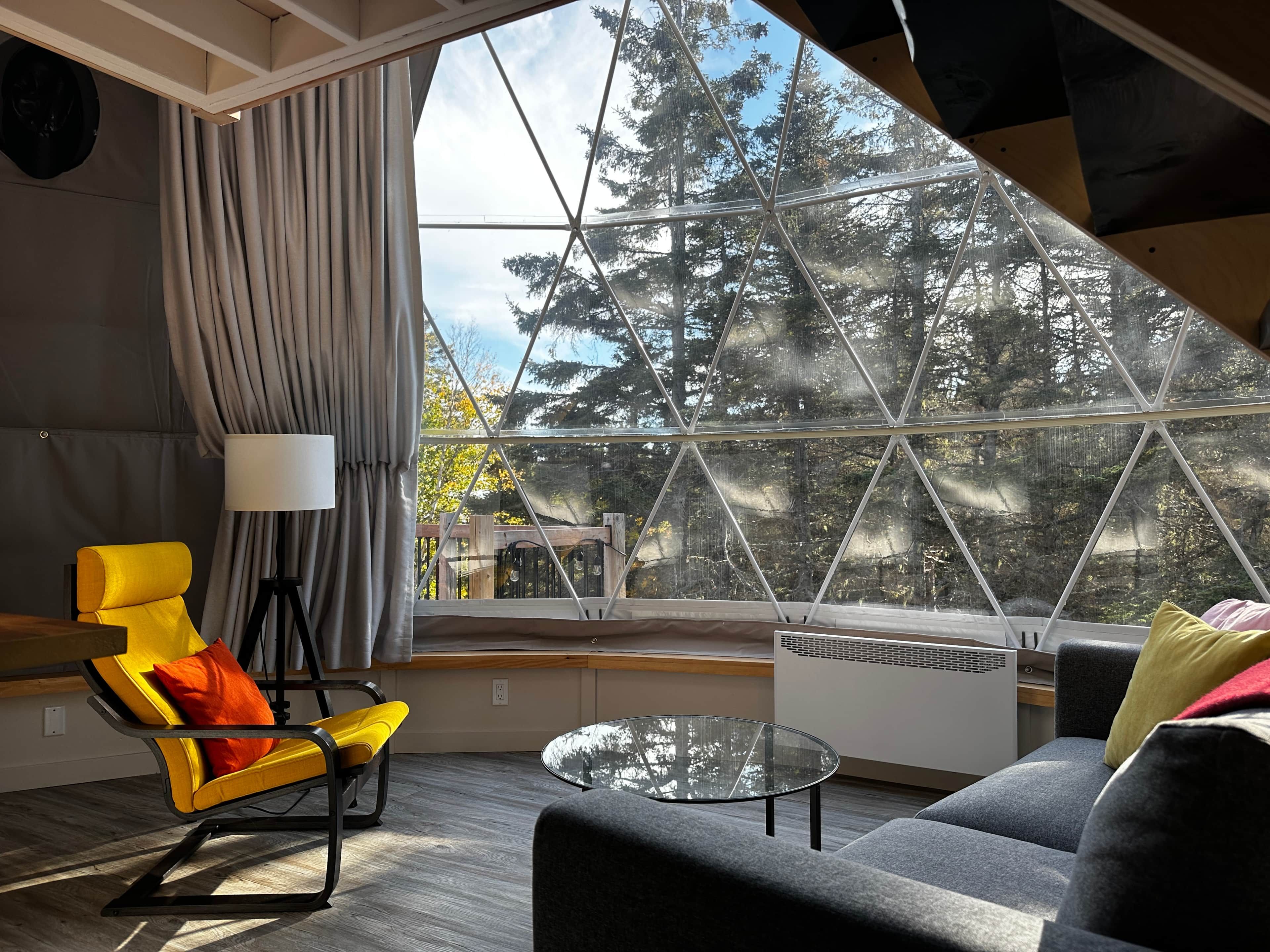 A modern interior with a large window, a yellow chair, a grey sofa, and a glass coffee table.
