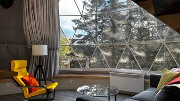 A modern interior with a large window, a yellow chair, a grey sofa, and a glass coffee table.
