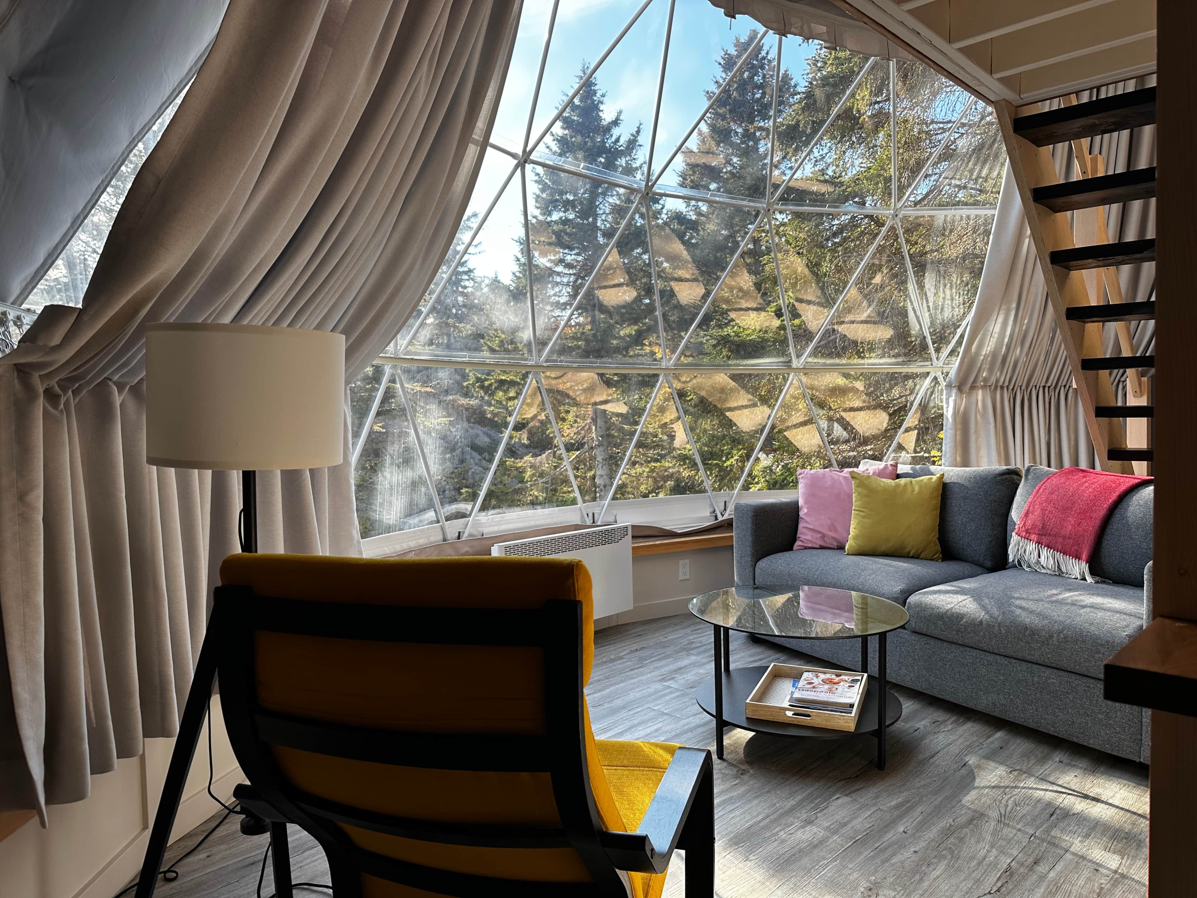 A cozy room with a large window, a sofa, a chair, a small table, and a bookshelf.