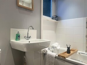 Une salle de bain avec un lavabo blanc, un miroir, un flacon de savon liquide, une serviette et un plateau en bois.