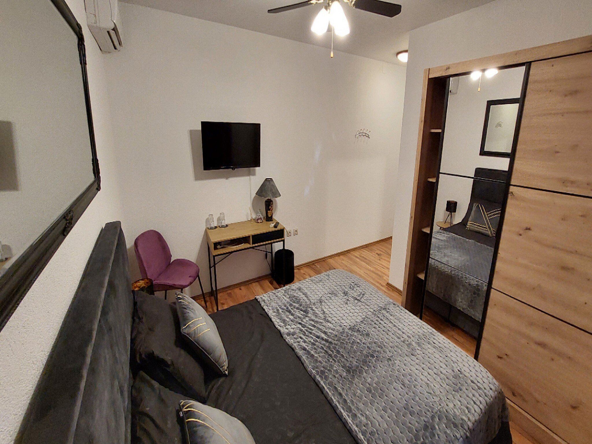 A bedroom with a bed, a desk, a chair, a TV, and a wardrobe.