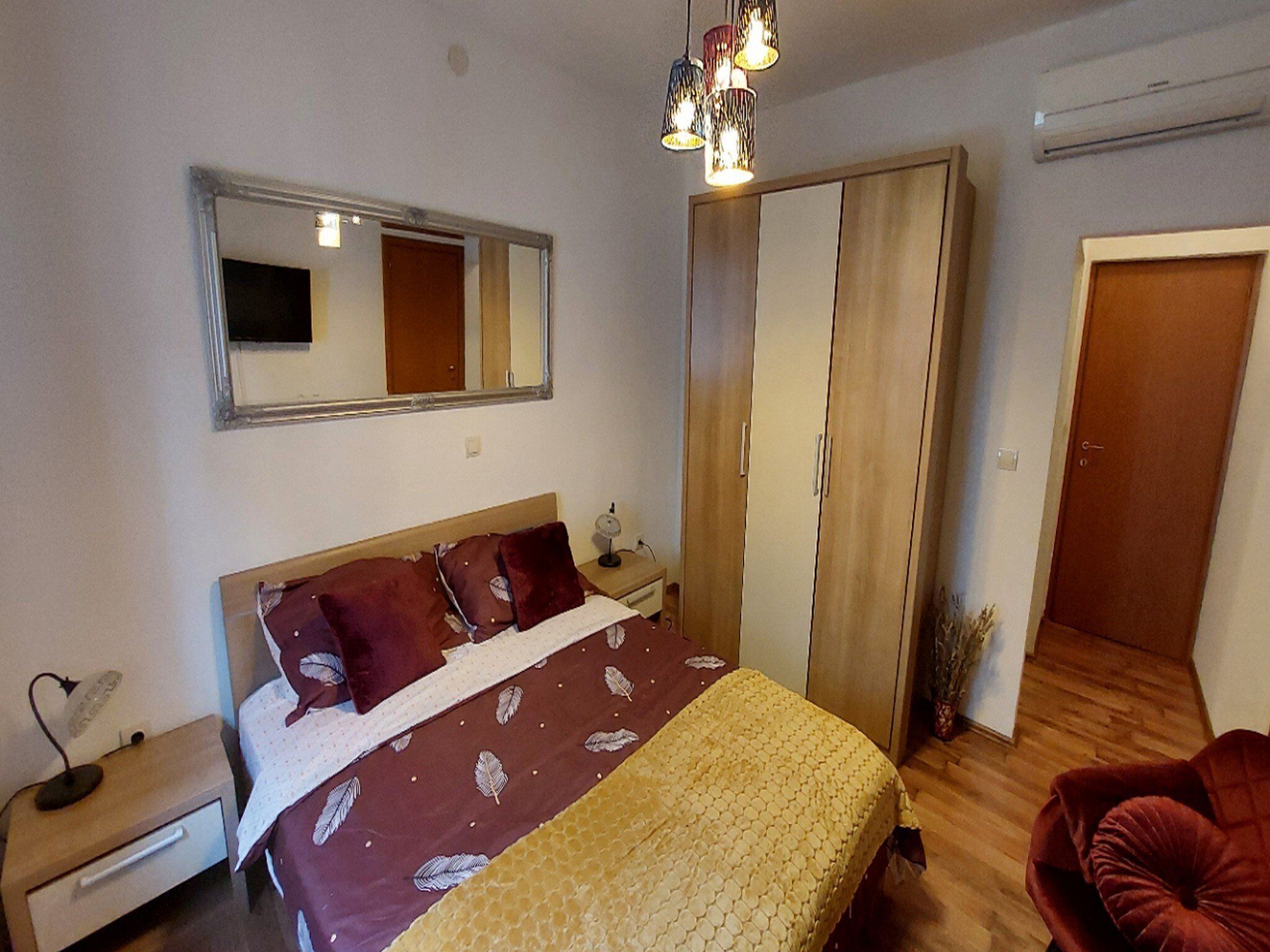 Un dormitorio con cama, armario, espejo, mesita de noche y una silla.