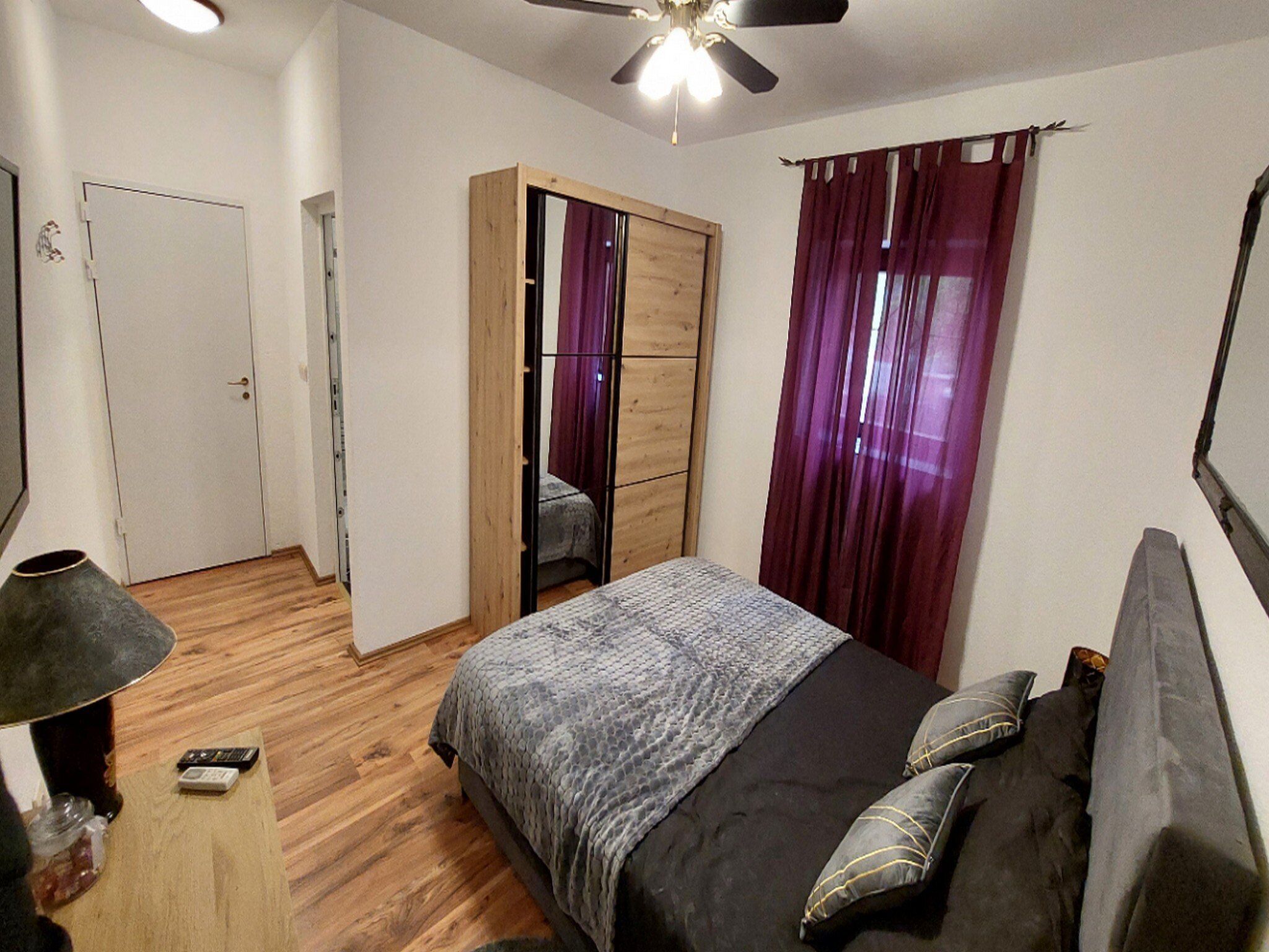 Un dormitorio con cama, armario, ventilador de techo y ventana con cortinas.